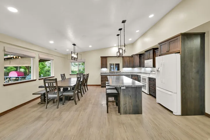Vaulted ceilings, recessed lighting, wood-finish flooring, dark wood cabinetry, and a kitchen island with seating