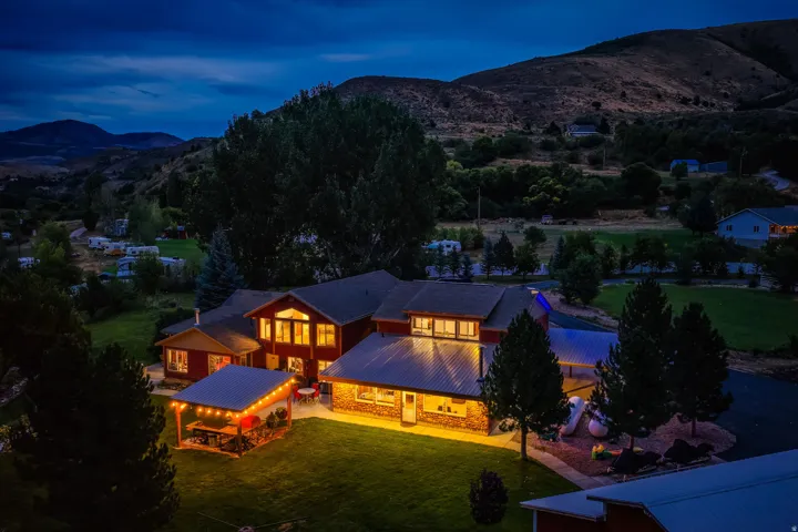 Red siding exterior with stone accents, featuring a covered patio structure, lush green lawn, and mature trees