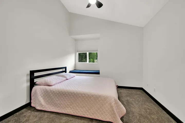 Sloped ceiling with an integrated ceiling fan, light gray walls, dark wood-finish flooring, built-in window bench, and an integrated window