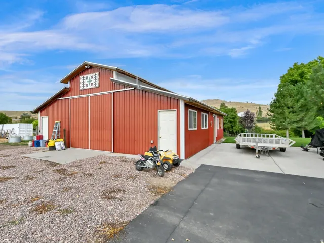 Red barn structure with white trim and windows, featuring a large gravel area and an asphalt driveway