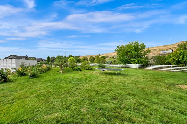 Expansive grassy lawn with a white fence, mature trees, and landscaping