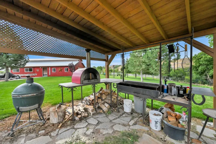Outdoor covered patio featuring a built-in outdoor kitchen, stone paver flooring, and a red barn-style structure in the background