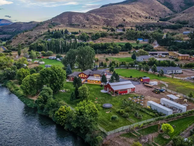 Riverfront property featuring a main residence, a large red barn, extensive green lawns, and a mountain backdrop