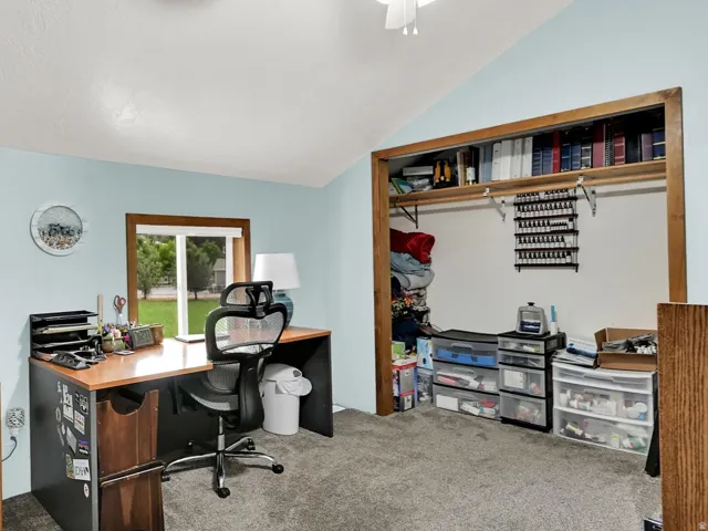 Vaulted ceiling with a ceiling fan, light blue wall paint, window with wood-finish trim, built-in closet, and gray carpet