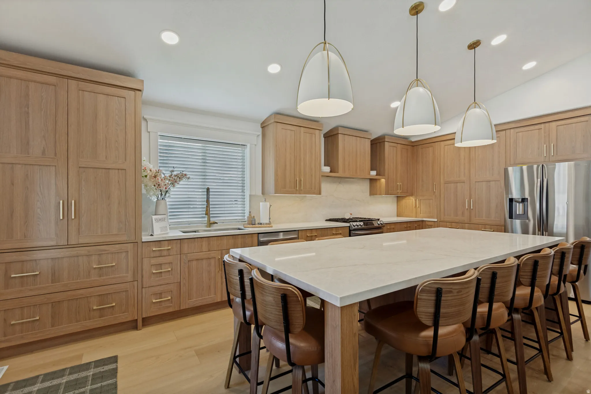 Spacious kitchen featuring extensive wood cabinetry, a large center island with a light-toned countertop, stainless steel appliances, and recessed lighting
