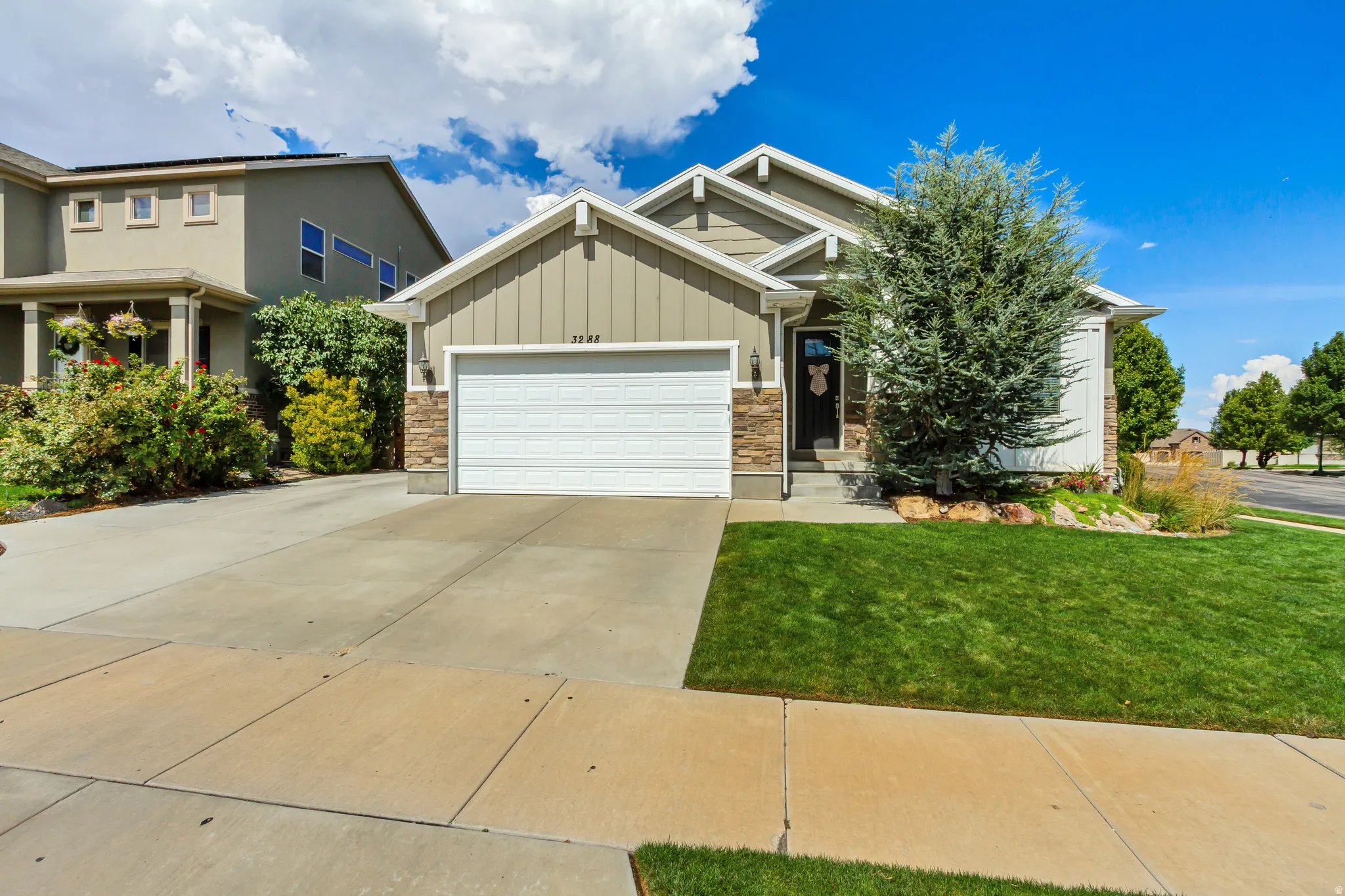 Exterior showcasing a combination of siding and stone veneer, a concrete driveway, an attached garage, and a landscaped front yard with a mature tree