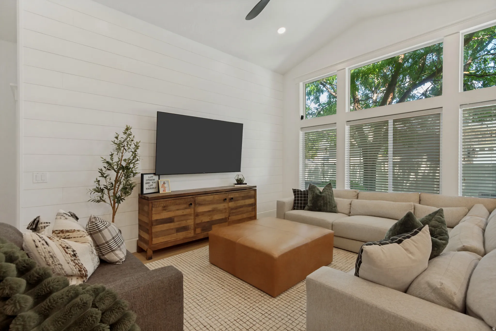Vaulted ceiling with a ceiling fan, expansive windows, shiplap accent wall, wood-finish flooring, and a built-in media console