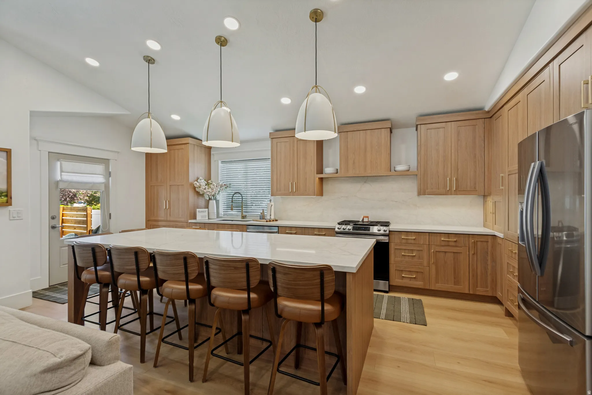 Vaulted ceiling with recessed lighting, large kitchen island with counter seating, wood-finish cabinetry, stainless steel appliances, and wood-finish flooring
