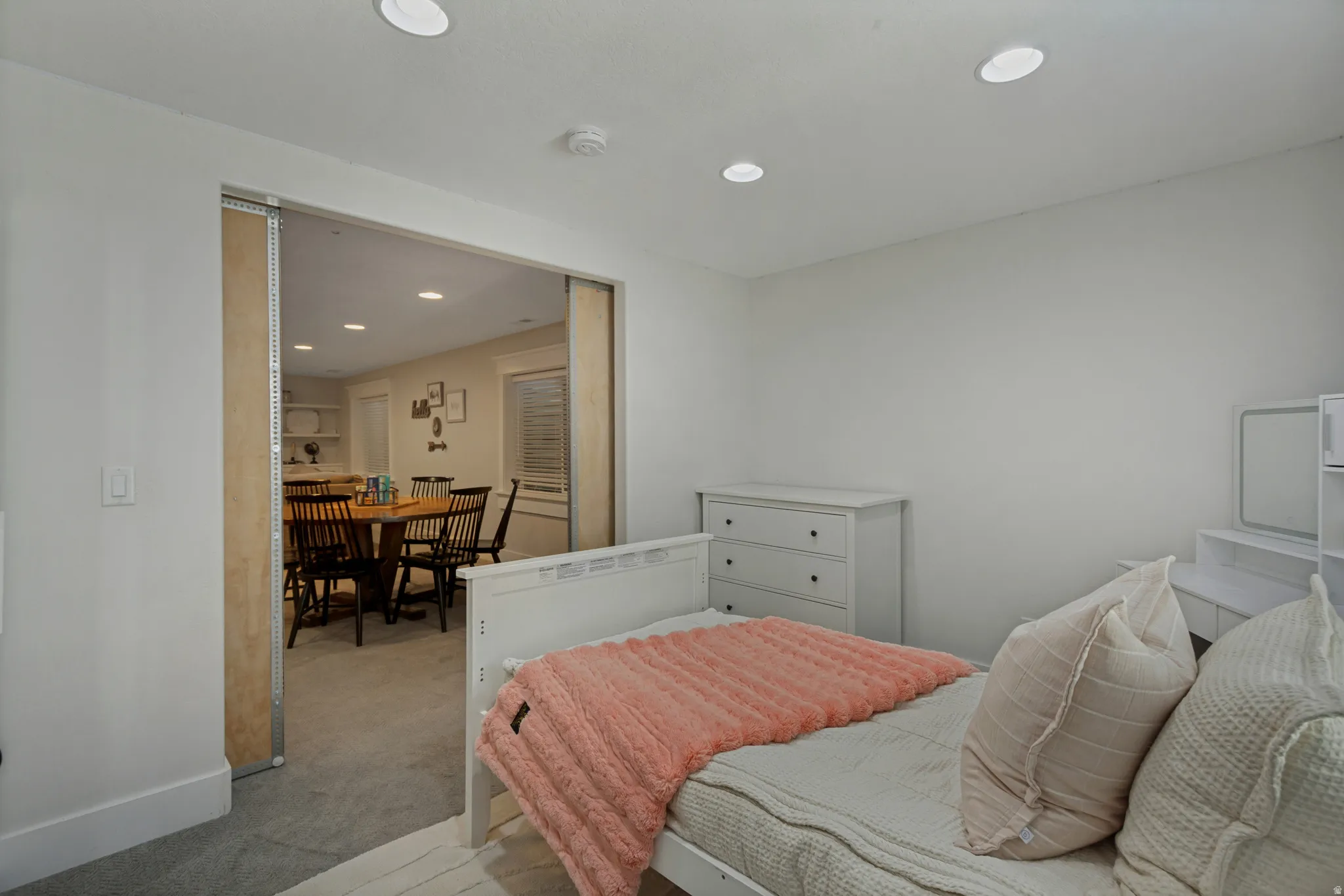 Recessed lighting illuminates the carpeted room, featuring white walls and a wide doorway opening to an adjacent space
