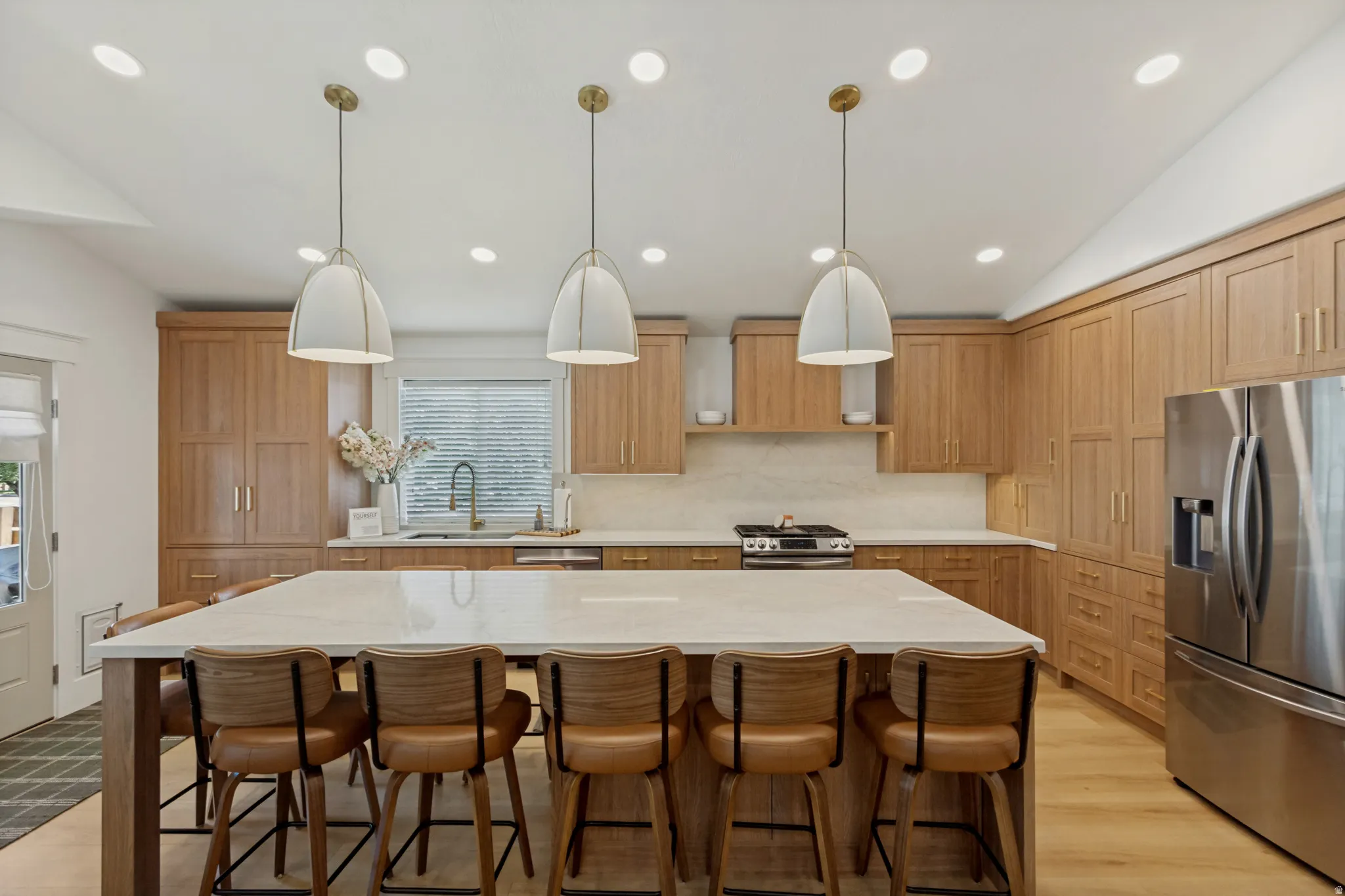 Kitchen featuring extensive wood cabinetry, a large center island with a light-toned countertop, stainless steel appliances, and recessed and pendant lighting