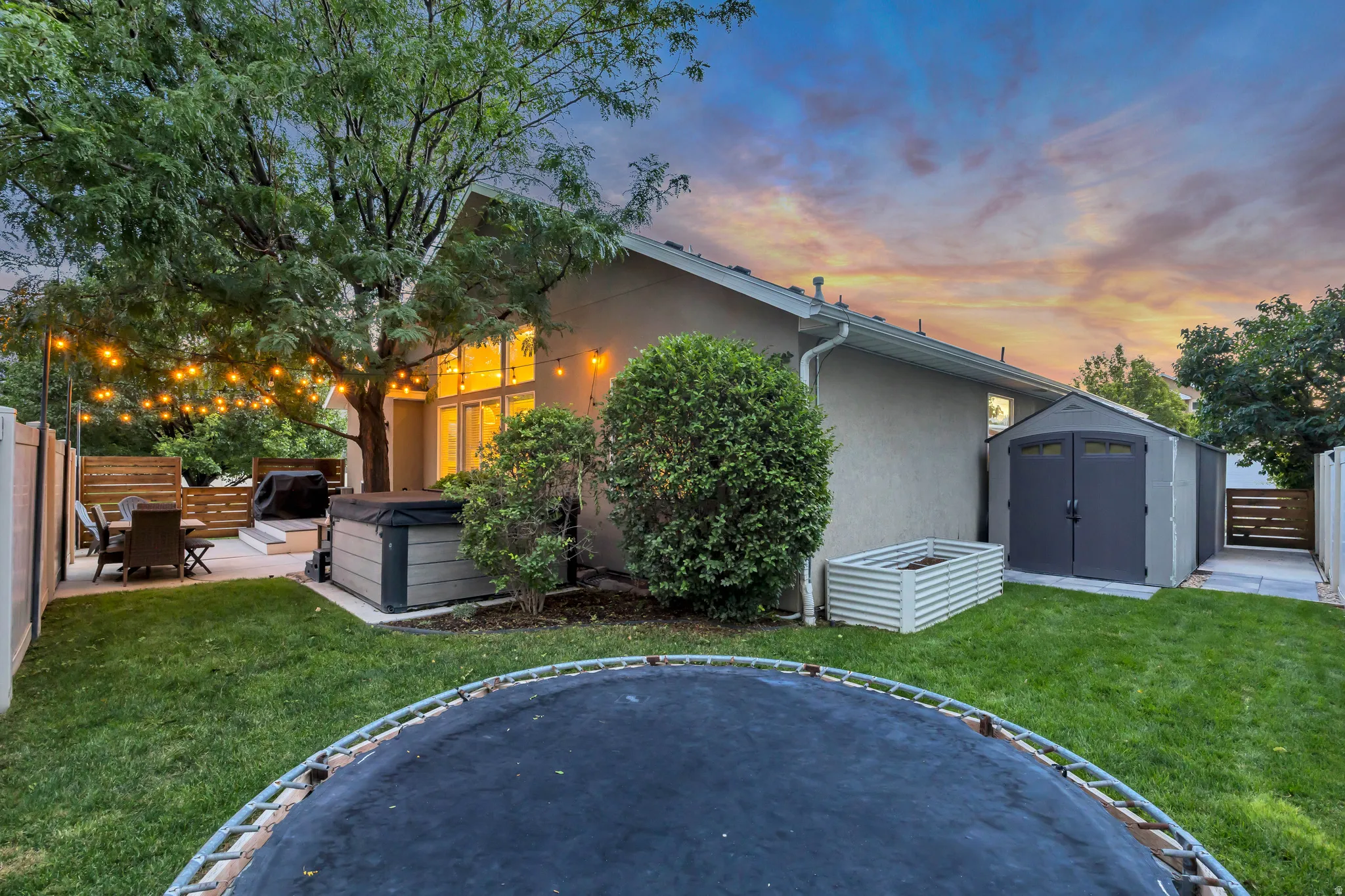 Expansive backyard featuring a manicured lawn, a concrete patio, a hot tub, and a storage shed