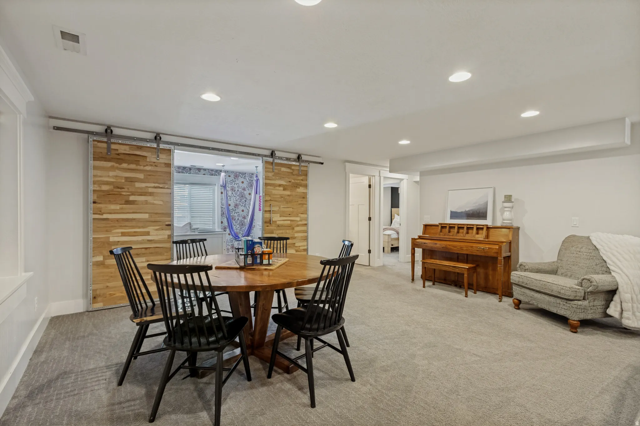 Recessed lighting, light gray carpeting, crisp white walls, and a wood-finish barn door