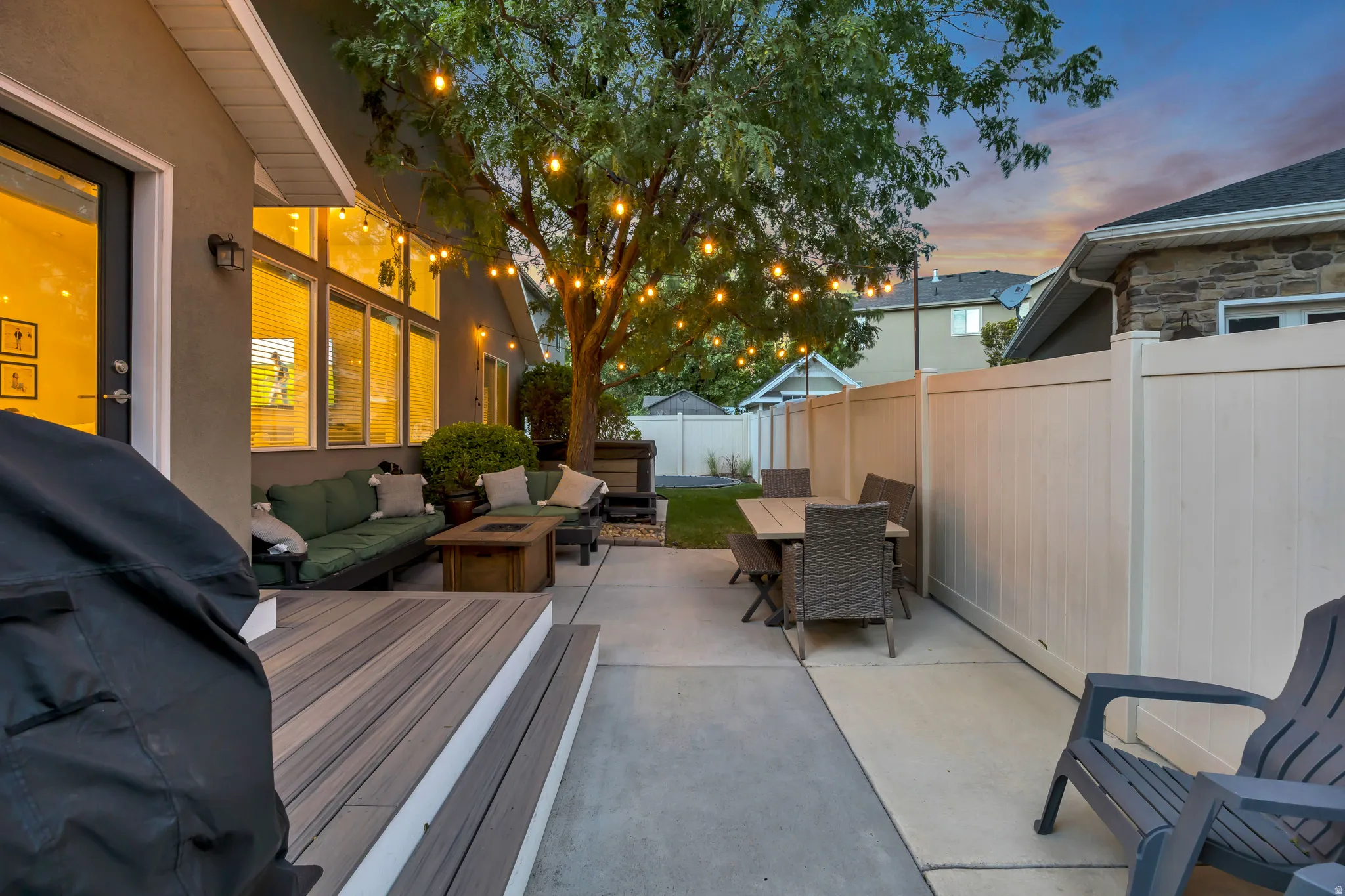 Expansive concrete patio with a composite deck, string lighting, and a privacy fence