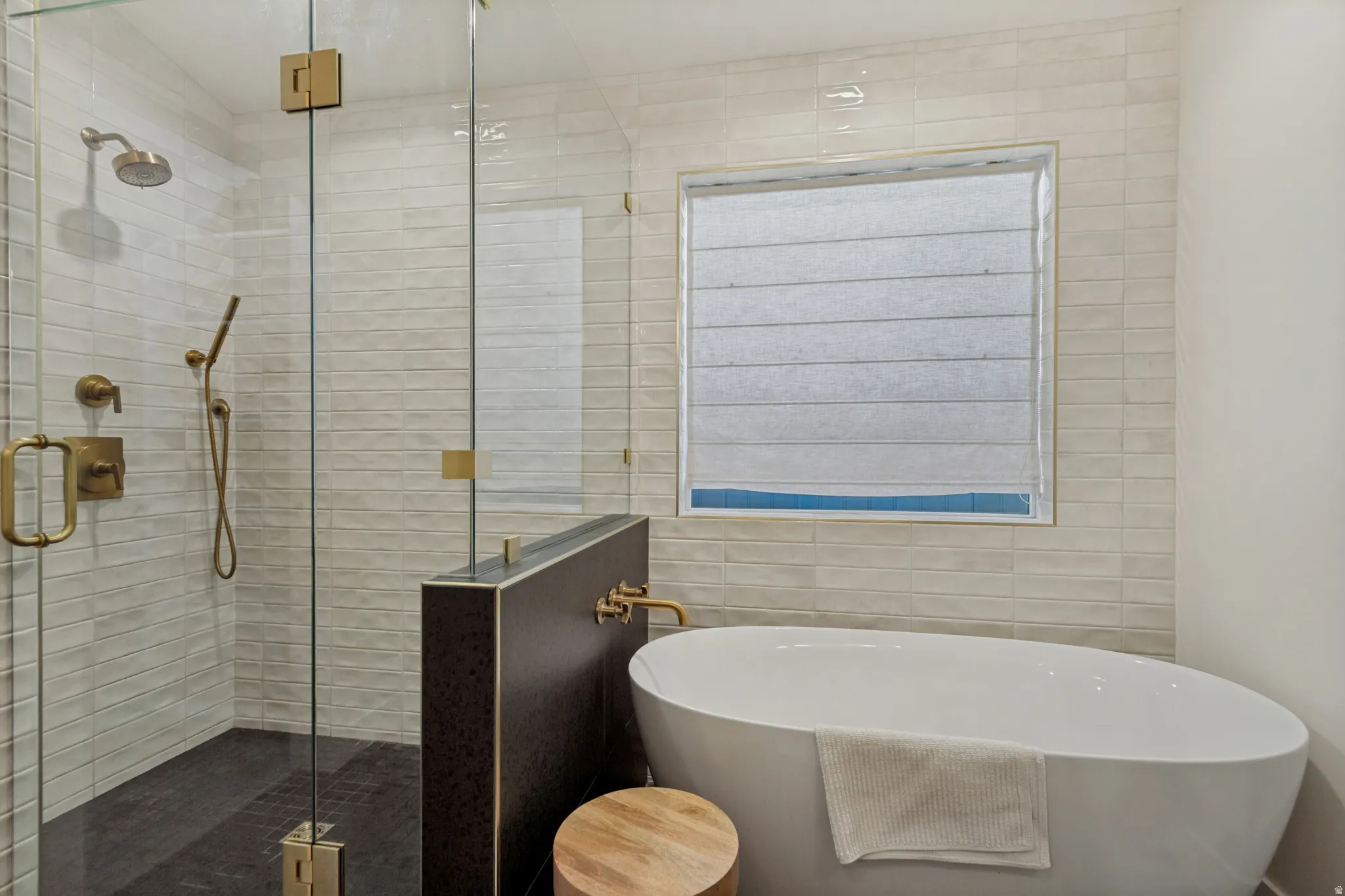 Glass-enclosed shower with gold-tone fixtures, freestanding soaking tub, and subway tile surround