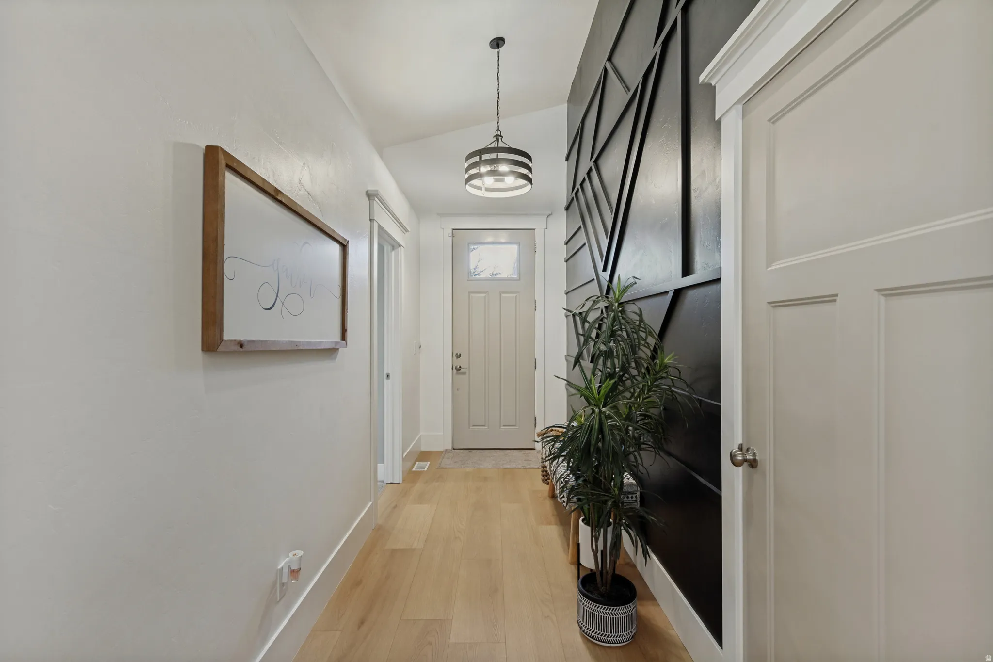 Wood-finish flooring, accent wall with geometric paneling, paneled interior doors, and a decorative pendant light fixture