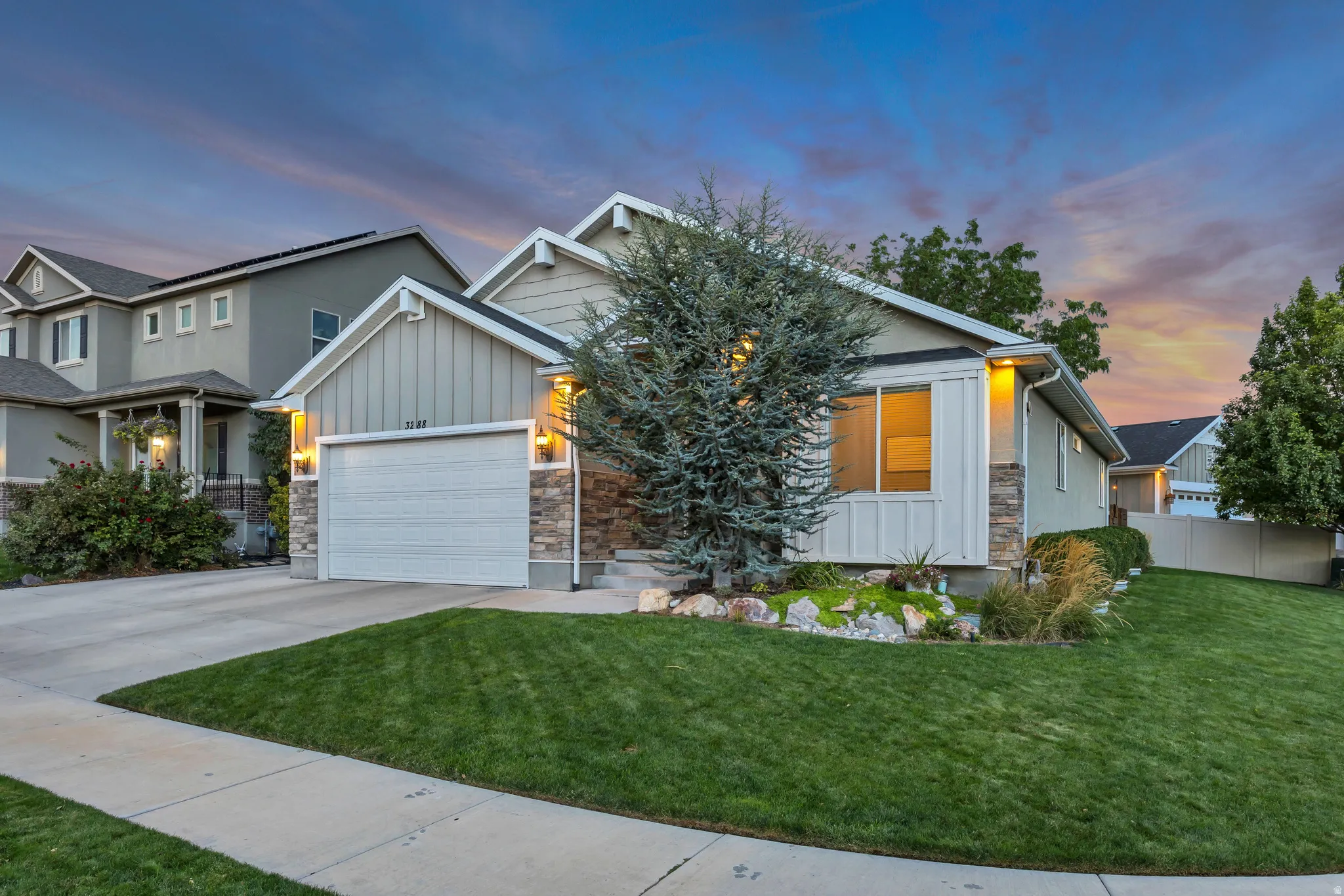 Concrete driveway with an integrated garage, stone veneer siding, and a landscaped front yard