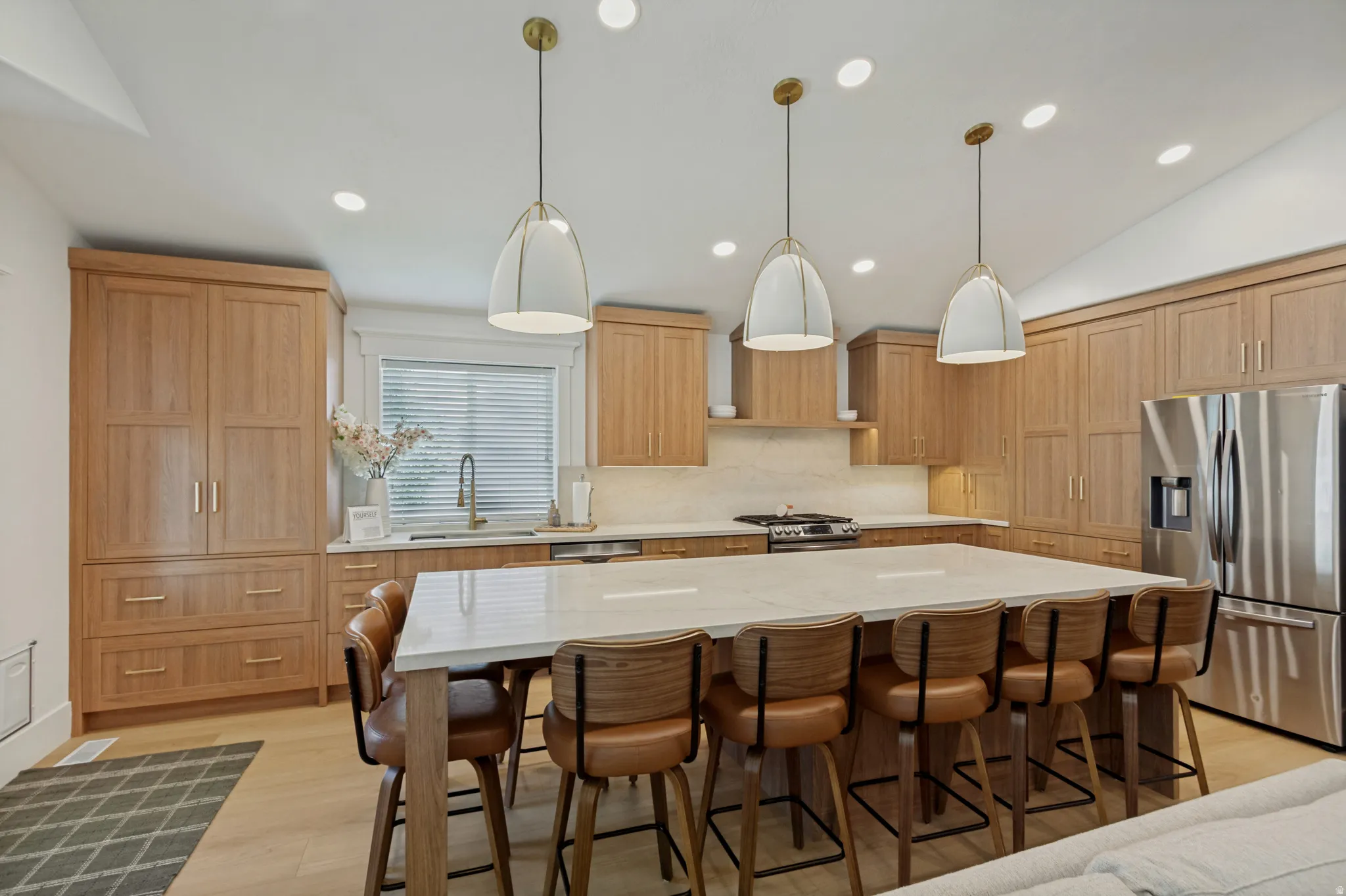 Spacious kitchen featuring light wood cabinetry, a large center island with seating, stainless steel appliances, and recessed and pendant lighting