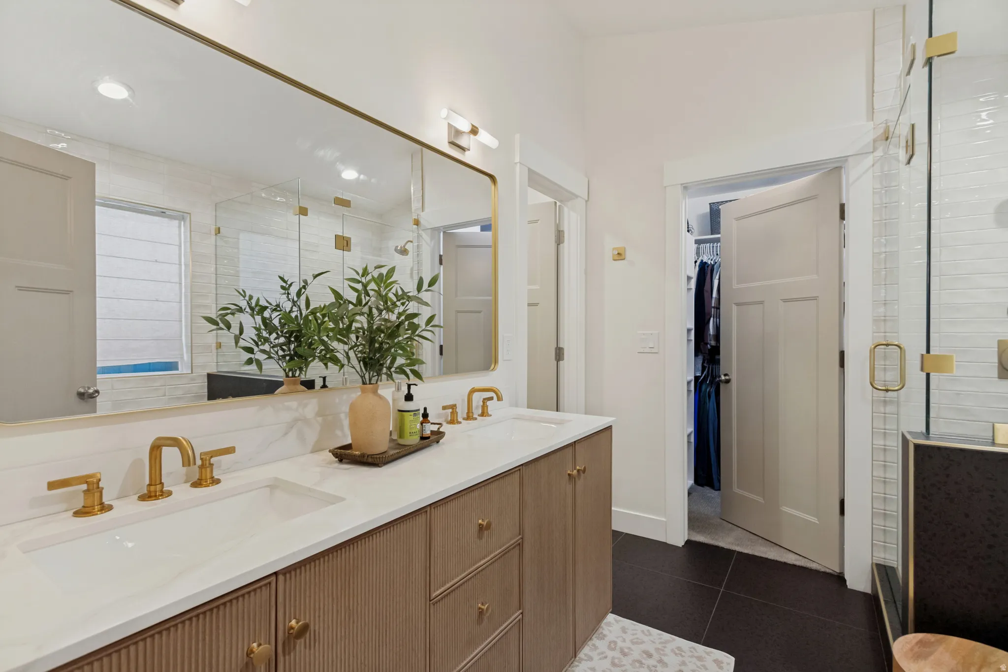 Spa-inspired primary bathroom featuring a wood-finish vanity with dual sinks, white quartz countertops, and brass hardware