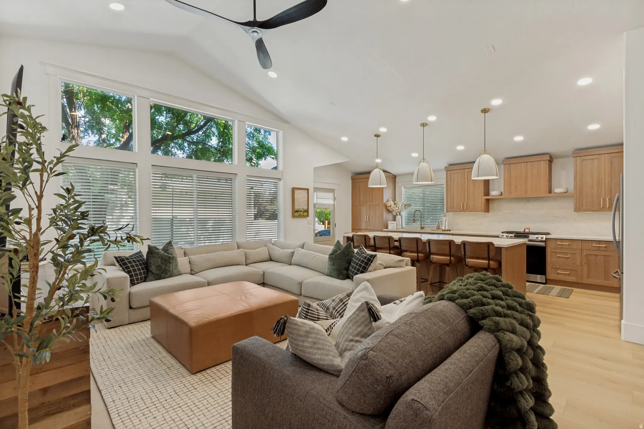 Vaulted ceiling with a ceiling fan, wall of windows, recessed lighting, wood-finish flooring, and a kitchen featuring light wood cabinetry