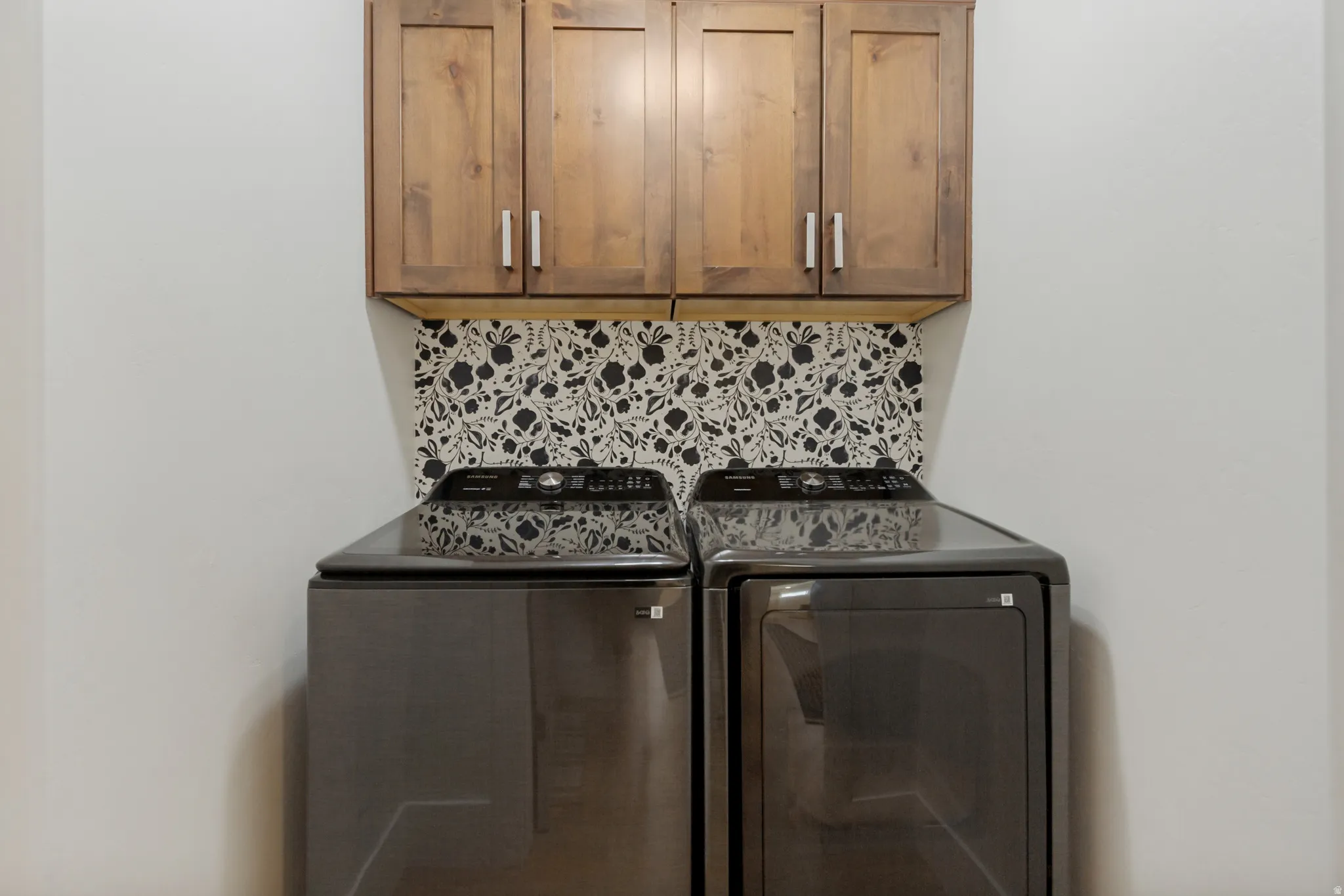 Wood-finish upper cabinetry with brushed nickel hardware and a decorative patterned backsplash