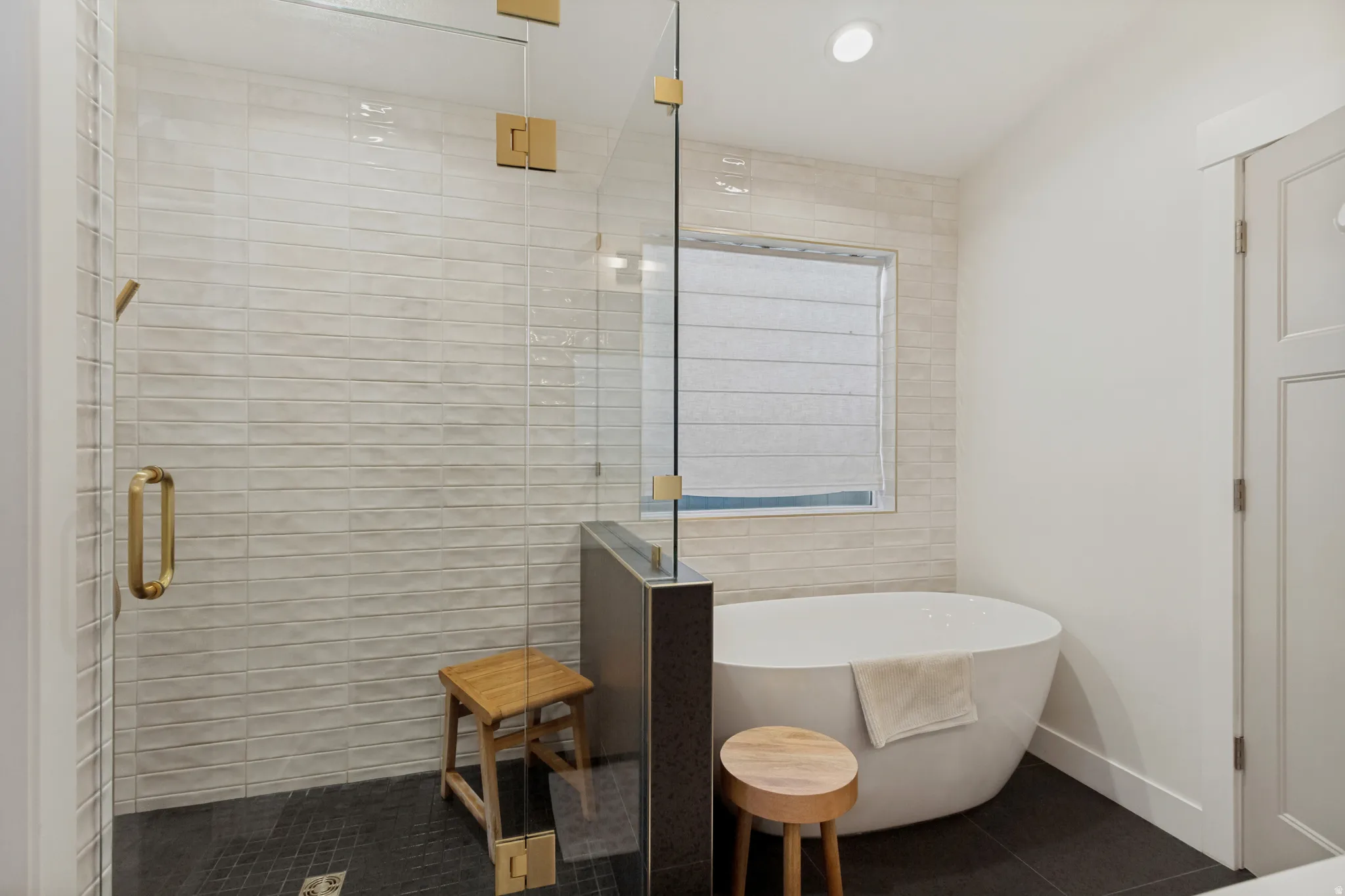 Freestanding soaking tub, glass-enclosed shower, gold-finish hardware, textured tile shower surround, and dark-toned floor tiles