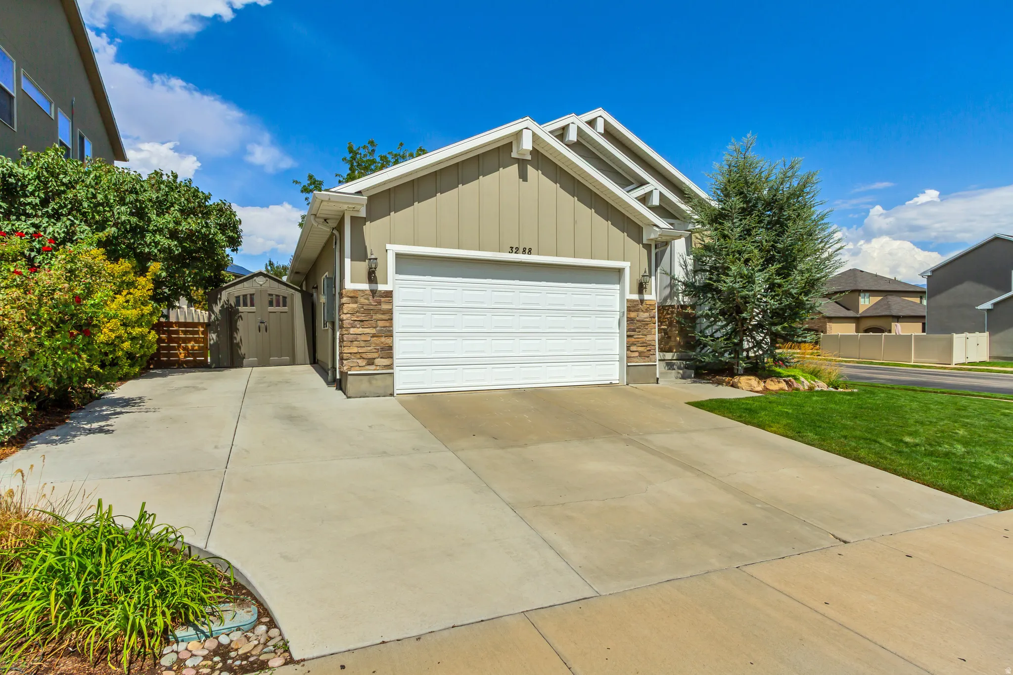 Driveway with attached garage, stone facade accents, and mature landscaping