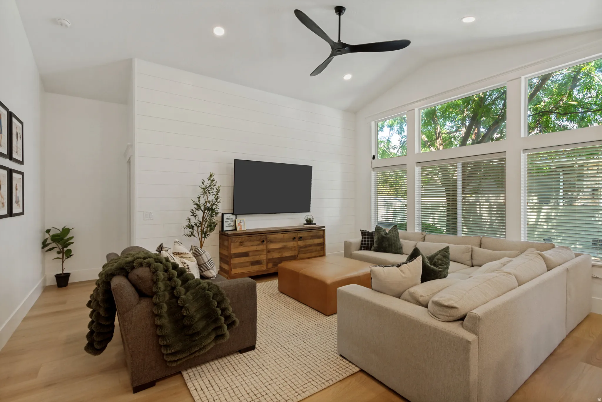 Vaulted ceiling with a contemporary ceiling fan, expansive windows, wood-finish flooring, and shiplap accent wall