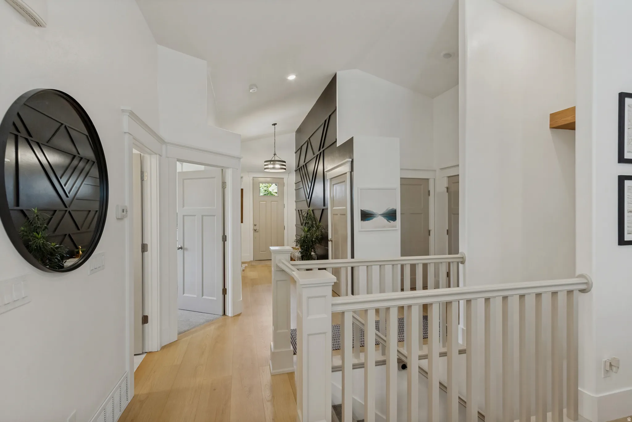 Hardwood-finish flooring, white painted balusters and handrails, an entryway pendant light, a wood accent shelf, and paneled interior doors