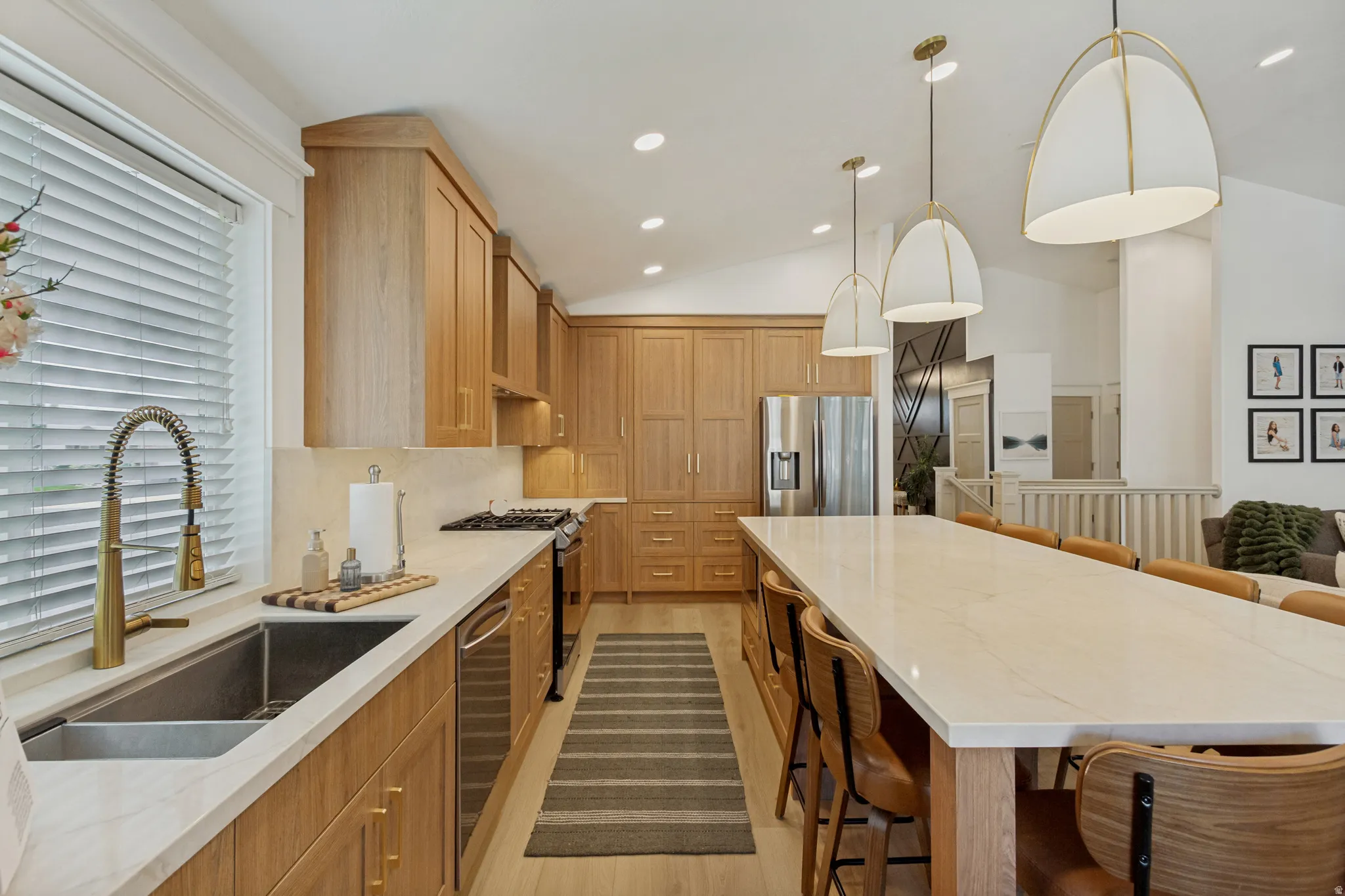Expansive kitchen featuring wood cabinetry, stainless steel appliances, a large center island with seating, recessed lighting, and decorative pendant light fixtures
