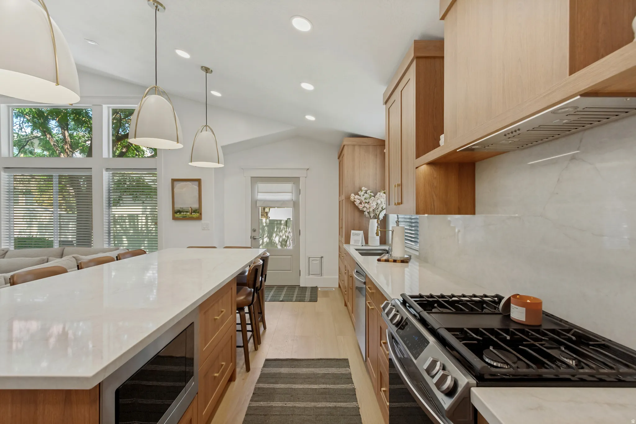Vaulted ceilings with recessed lighting, large windows, wood-finish cabinetry, stainless steel appliances, and a gas range