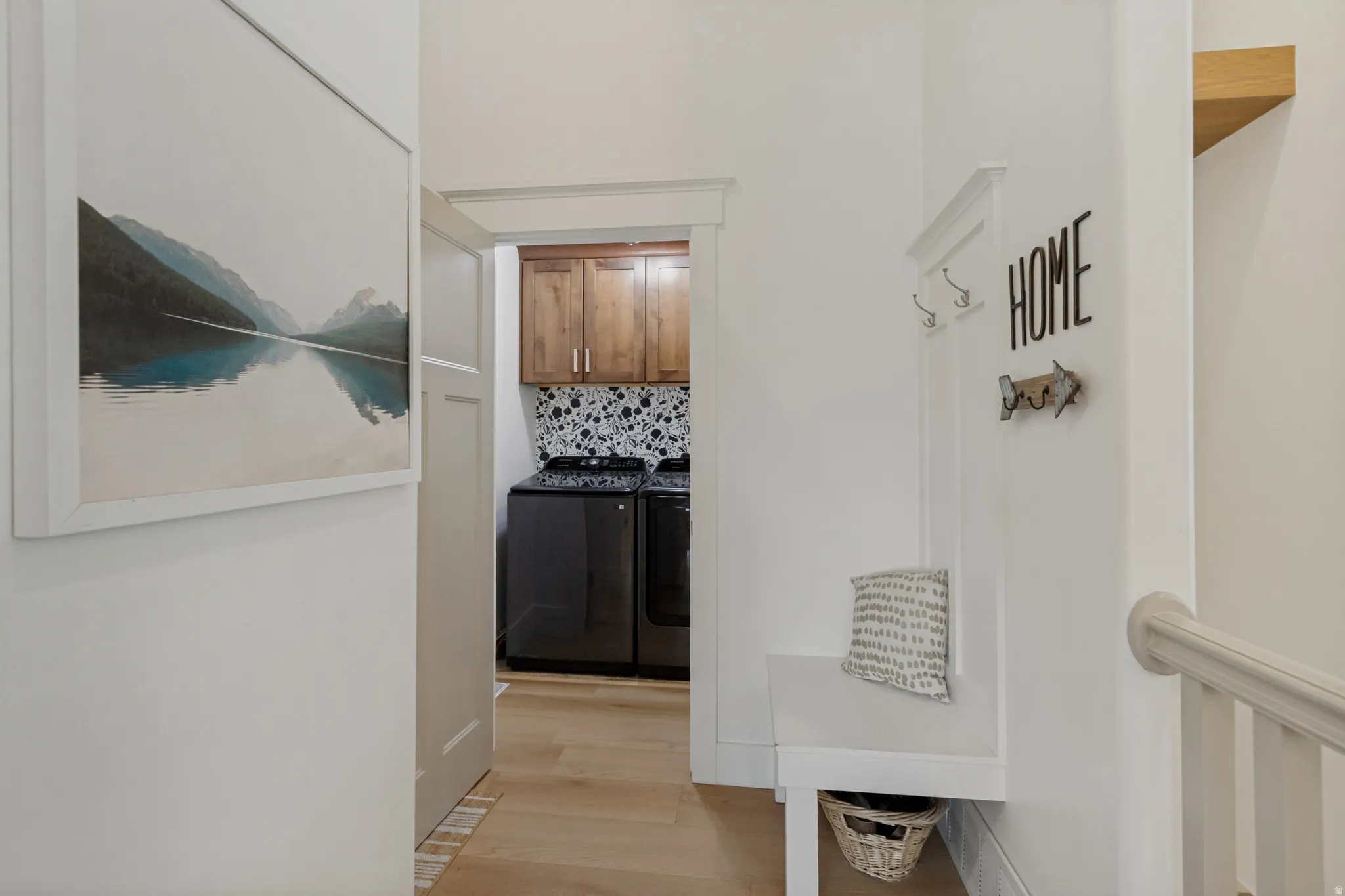 Dedicated laundry area featuring wood-finish flooring, patterned tile backsplash, and upper wood cabinetry