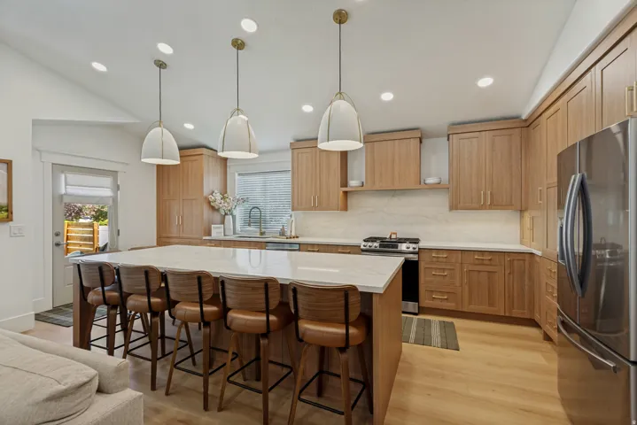 Vaulted ceiling with recessed lighting, large kitchen island with counter seating, wood-finish cabinetry, stainless steel appliances, and wood-finish flooring