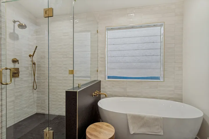 Glass-enclosed shower with gold-tone fixtures, freestanding soaking tub, and subway tile surround