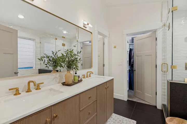 Spa-inspired primary bathroom featuring a wood-finish vanity with dual sinks, white quartz countertops, and brass hardware
