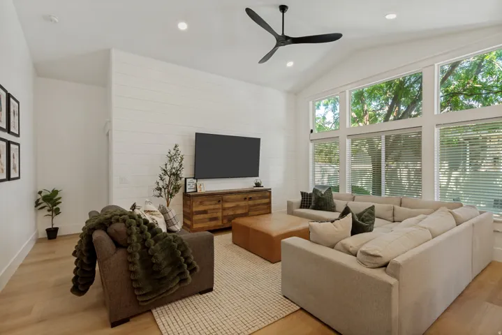 Vaulted ceiling with a contemporary ceiling fan, expansive windows, wood-finish flooring, and shiplap accent wall