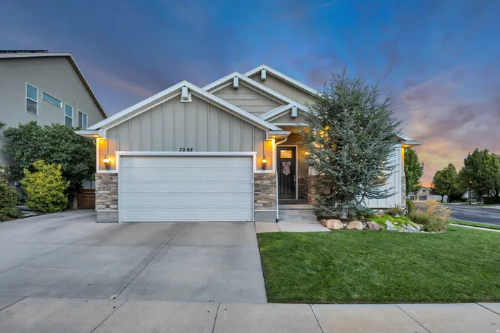 Exterior featuring vertical siding and stone accents, a concrete driveway, an attached garage, a manicured lawn, and mature landscaping