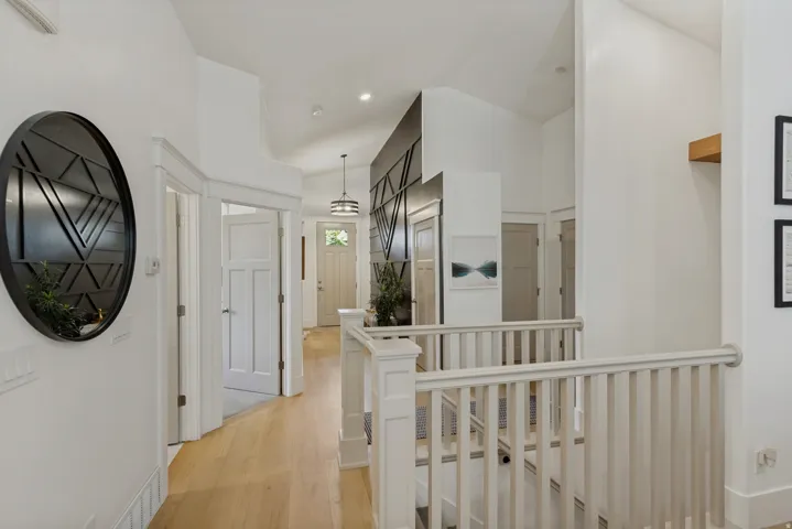 Hardwood-finish flooring, white painted balusters and handrails, an entryway pendant light, a wood accent shelf, and paneled interior doors