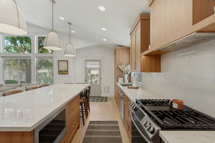 Vaulted ceilings with recessed lighting, large windows, wood-finish cabinetry, stainless steel appliances, and a gas range