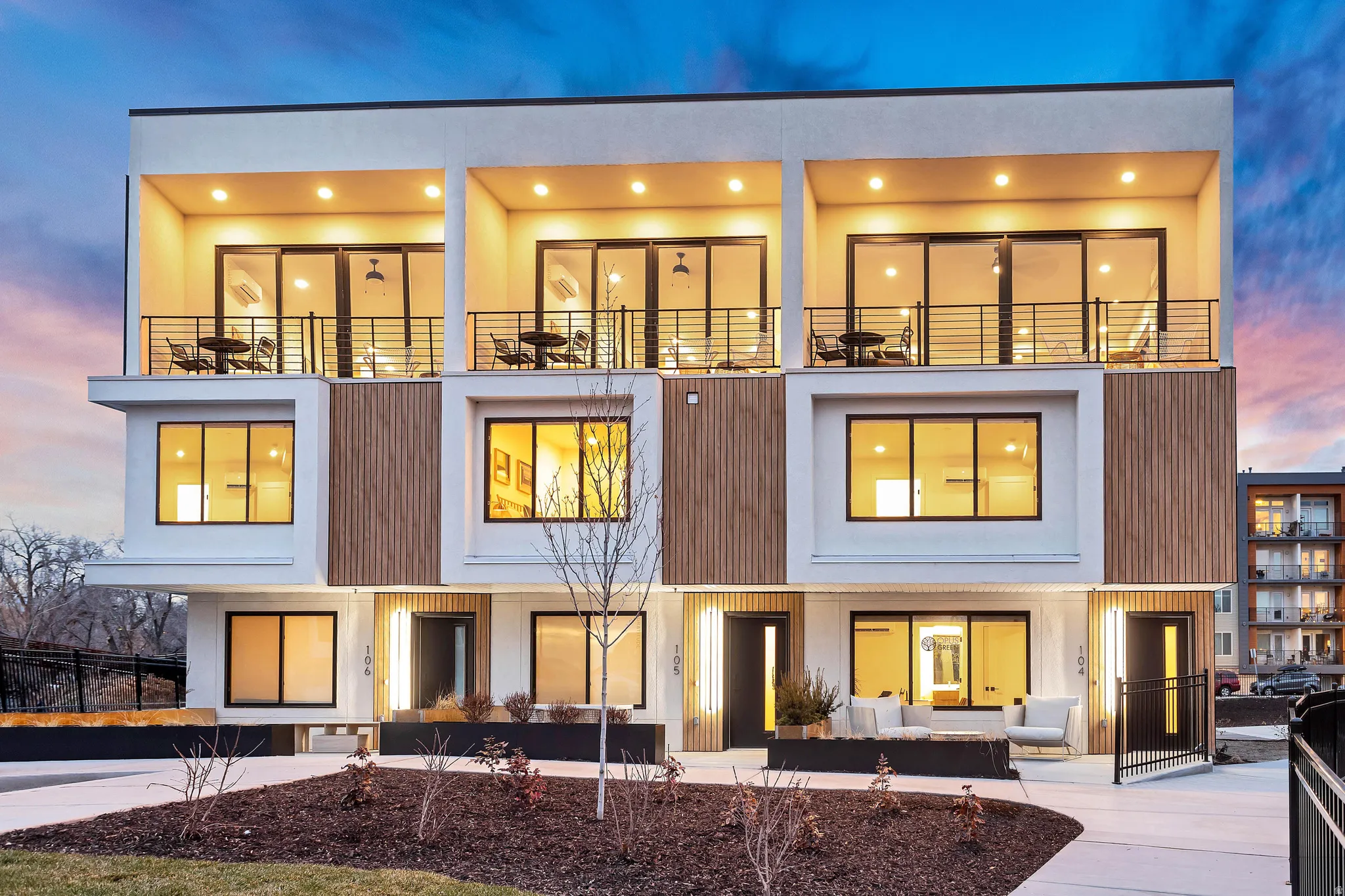 Modern multi-unit residential building featuring three stories of contemporary architecture with clean lines and mixed material façade combining white exterior panels and vertical wood-finish accents