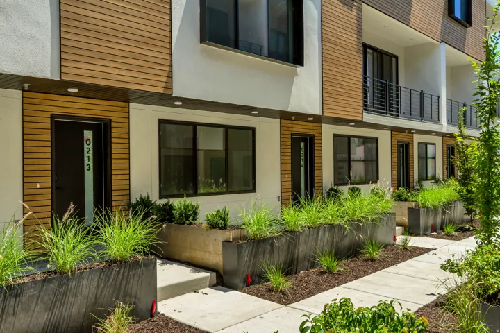 Contemporary multi-level facade featuring wood-finish siding, crisp white stucco, and a private balcony with black railings