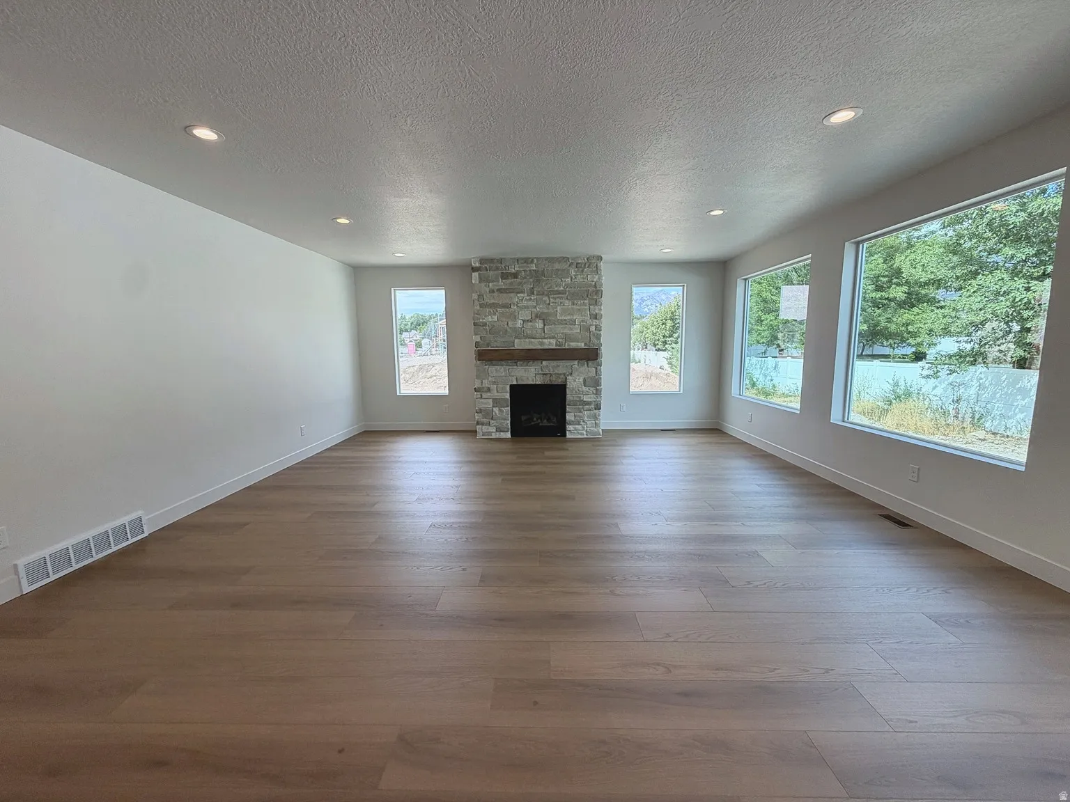 Wood-finish flooring, recessed lighting, and a stacked stone fireplace with a wood mantle