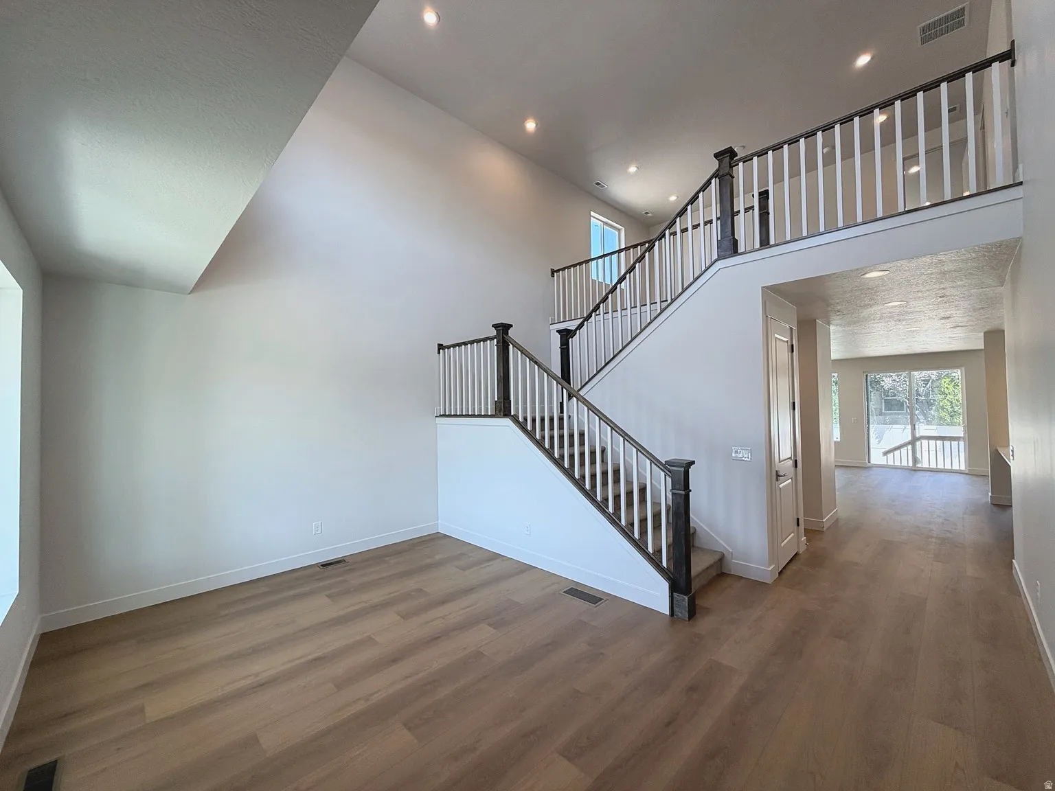 Vaulted ceiling with recessed lighting, wood-finish flooring, two-story staircase with dark newel posts and white spindles, and a light-filled interior