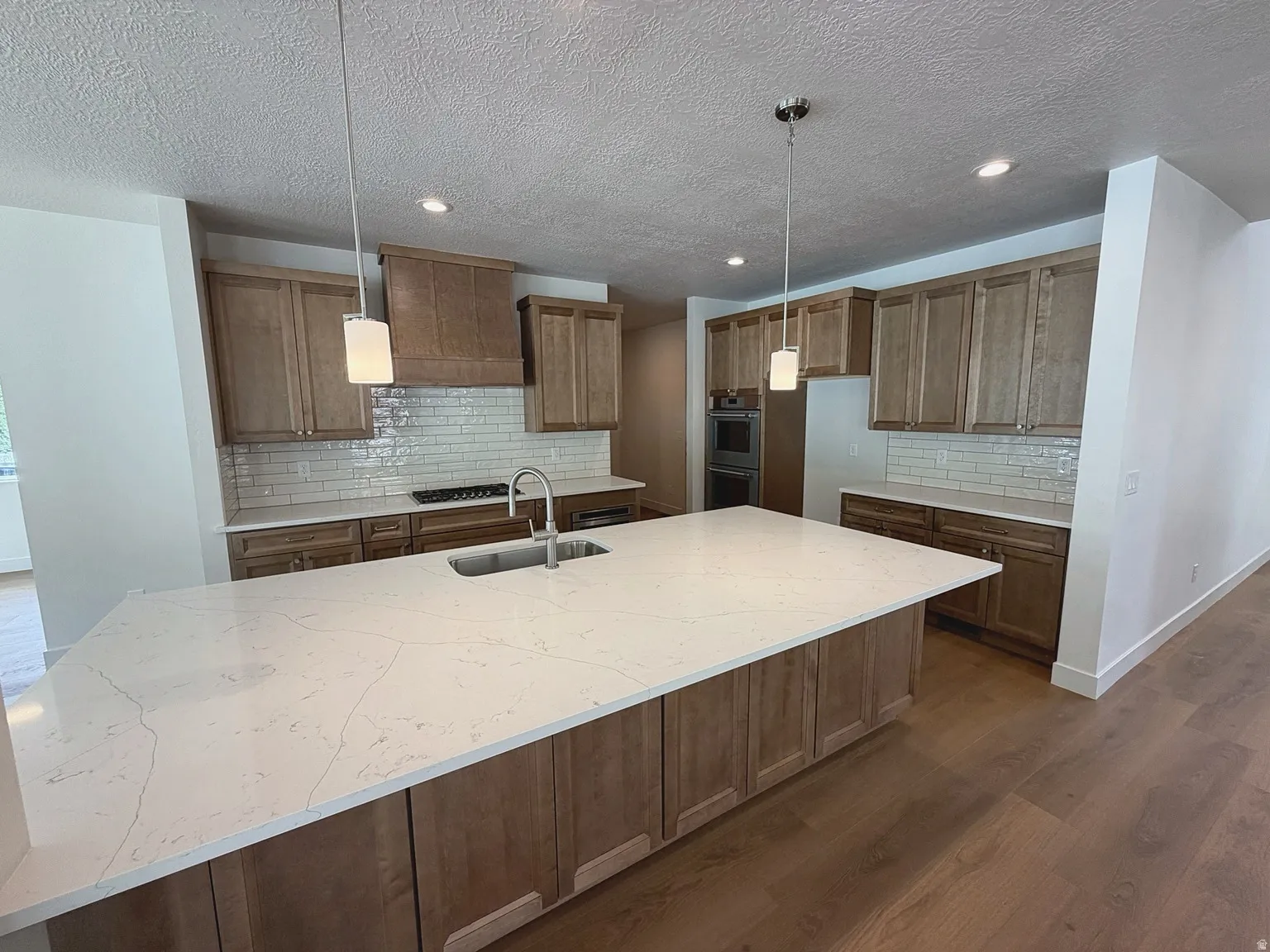 Spacious kitchen featuring a large island with a surface, wood-finish cabinetry, subway tile backsplash, and built-in appliances