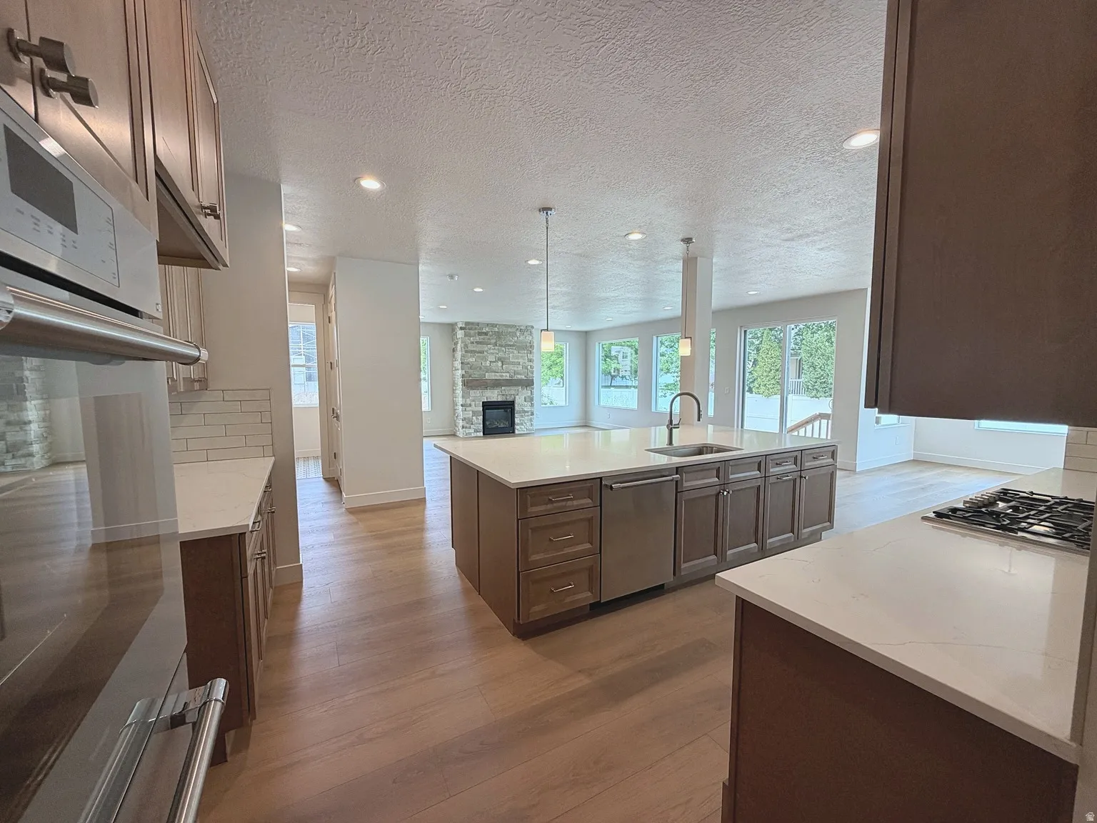 Kitchen featuring a gas range, built-in microwave, wood-finish flooring, an island with a sink, and pendant lighting