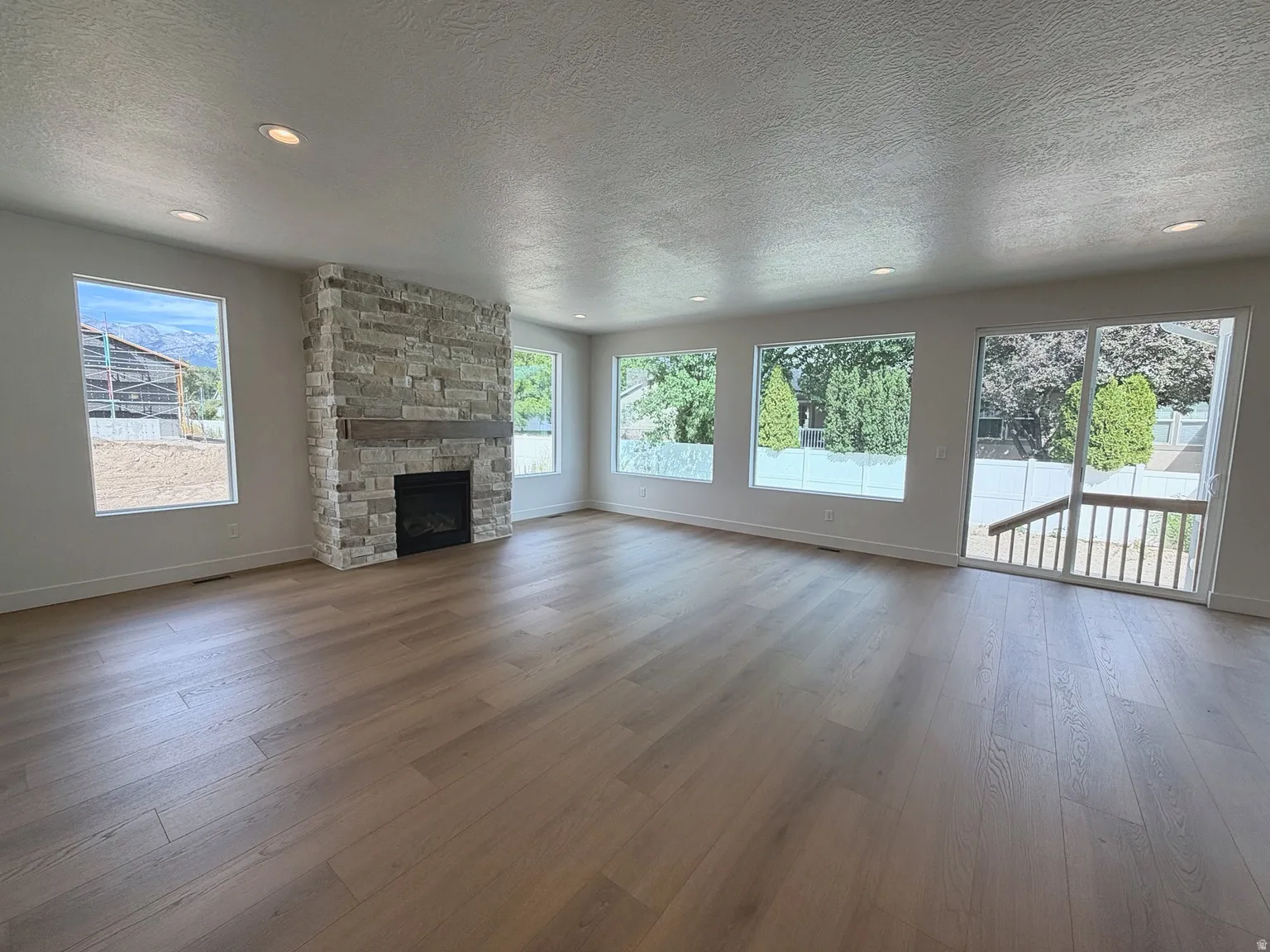 Spacious room featuring wood-finish flooring, a stone-faced fireplace with a wood mantle, recessed lighting, and multiple large windows