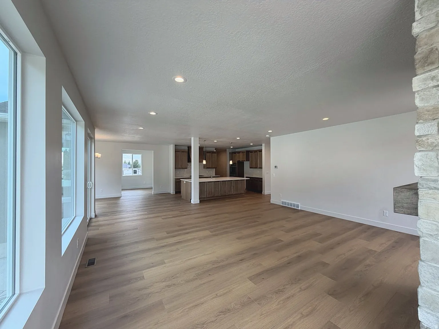 Expansive open-concept room featuring wood-finish flooring, recessed lighting, a stone fireplace surround, and multiple large windows