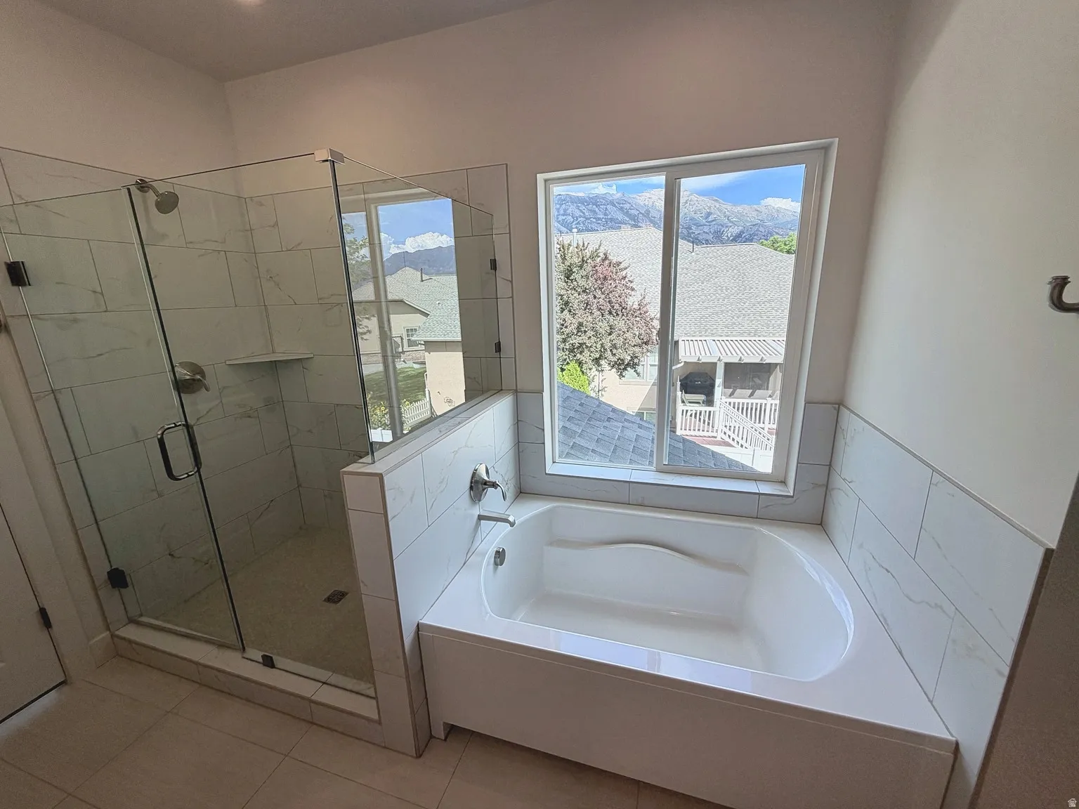 Full-size soaking tub with tiled surround, frameless glass shower enclosure, and tiled shower walls with built-in niche