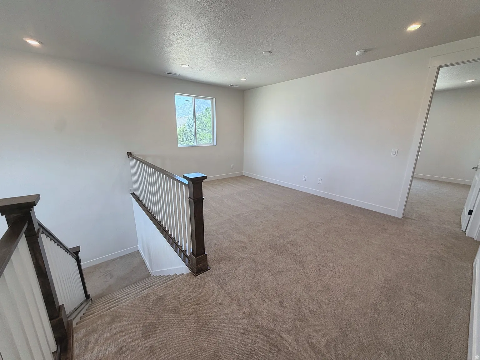 Expansive carpeted area with recessed lighting, a single window, and white walls