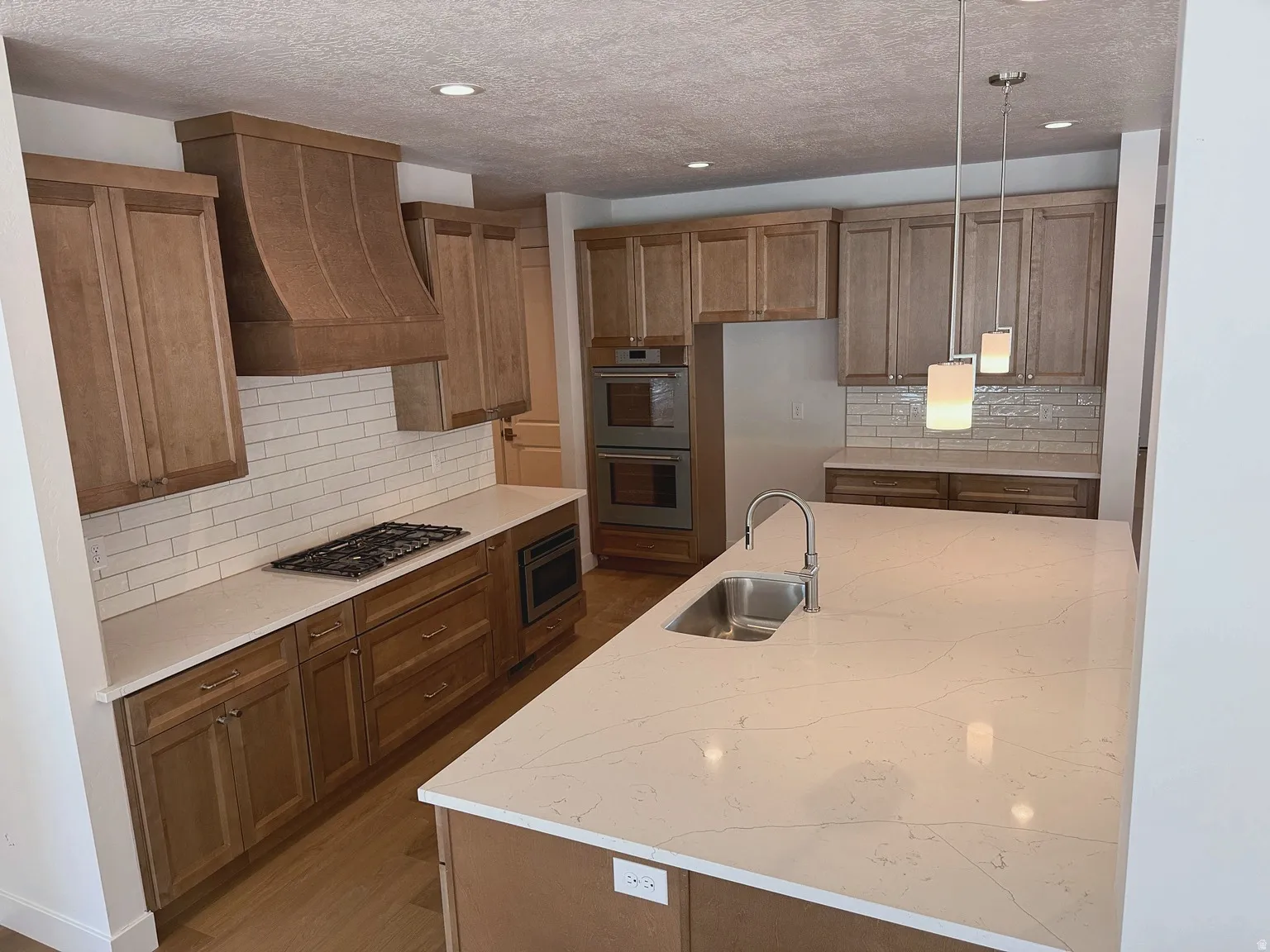 Gourmet kitchen featuring a center island with sink, wood cabinetry, built-in double oven, built-in microwave, and subway tile backsplash