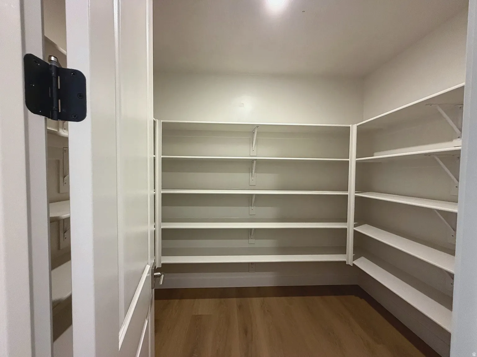Expansive walk-in pantry with wrap-around white shelving, wood-finish flooring, and recessed lighting